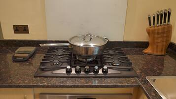 A kitchen with a stove, a pot on the burner, a knife block, and a digital clock displaying 12:00.