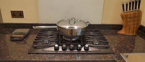 Una cocina con estufa, una olla en la hornilla, un bloque de cuchillos y un reloj digital que marca las doce.