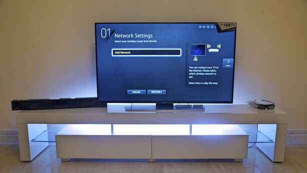 A flat-screen TV on a modern, white entertainment unit with a network settings menu displayed. - GGC Apartments (Lagos)