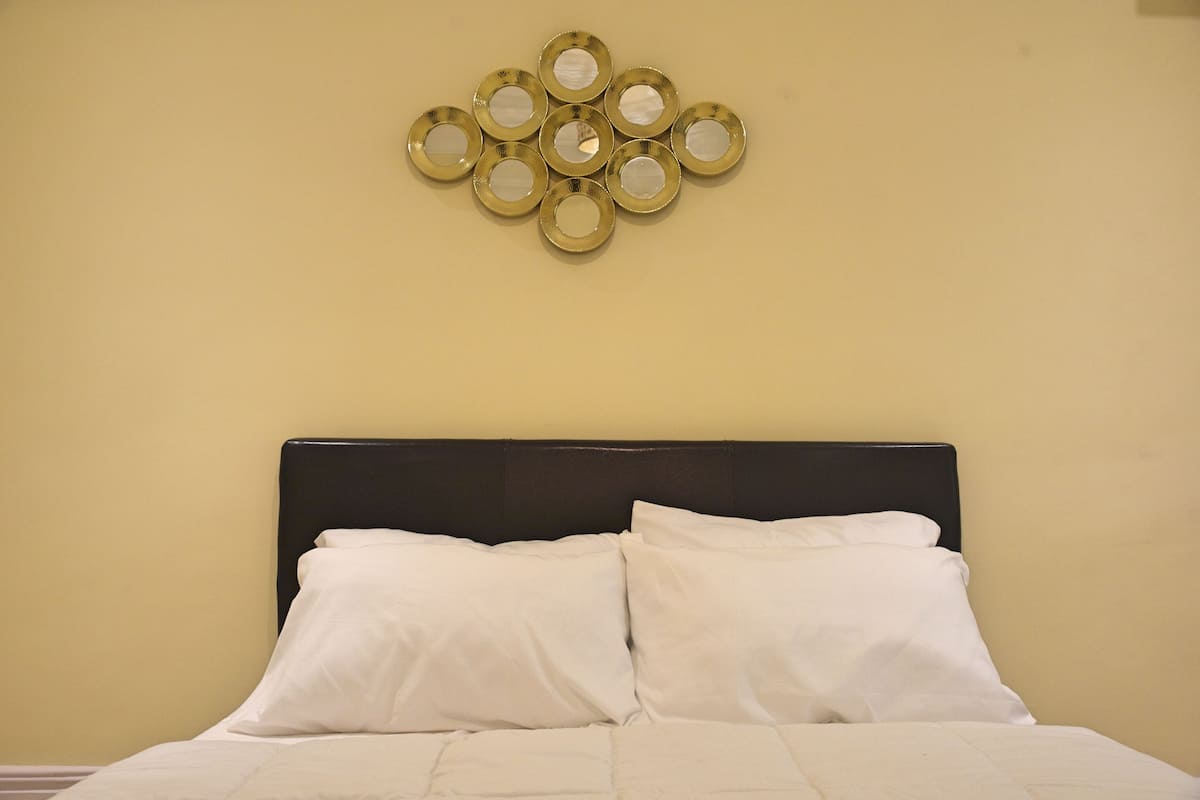 A bed with white bedding, a black headboard, and a wall-mounted circular mirror decoration.