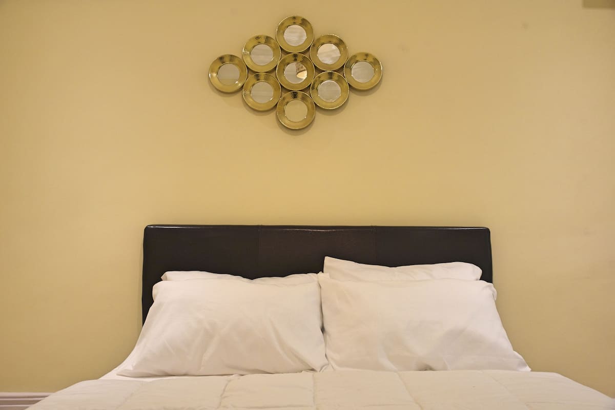 A bed with white linens and a black headboard, a wall-mounted circular mirror, and a plain wall.