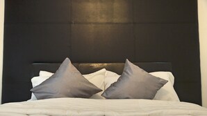 A neatly made bed with white bedding and two gray pillows. - GGC Apartments (Lagos)