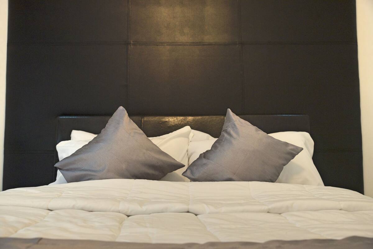 A neatly made bed with white bedding and two gray pillows.