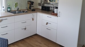 Una cocina compacta con armarios blancos, un microondas, un lavamanos y una cafetera.