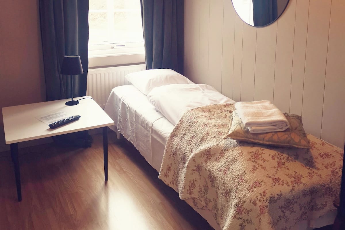 Ein kleiner, ordentlich eingerichteter Raum mit einem Bett, einem Schreibtisch und einem Spiegel.