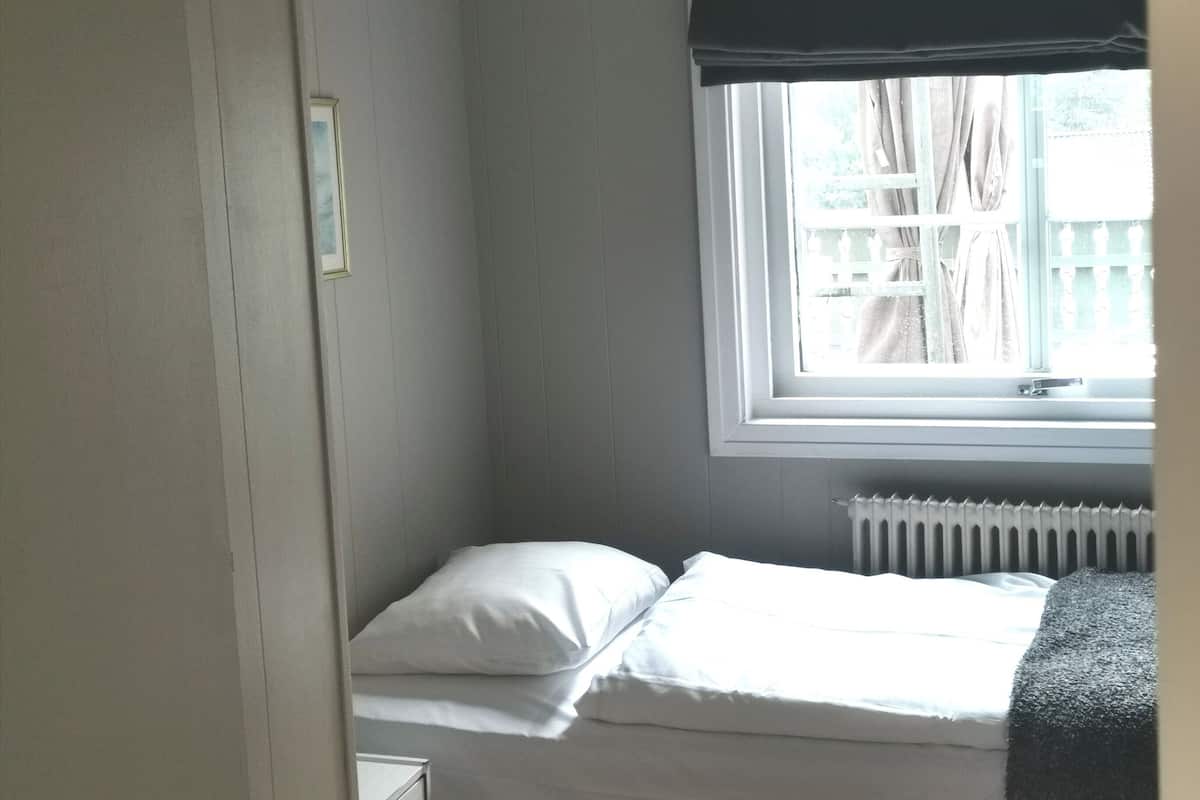 Ein kleines Zimmer mit einem Einzelbett, einem Fenster, einer Heizung und einem Nachttisch.