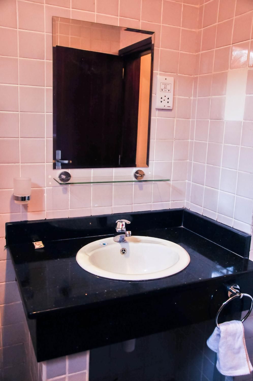 Un baño con encimera negra, lavamanos blanco, espejo y toallero.