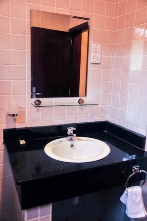 Un baño con encimera negra, lavamanos blanco, espejo y toallero.