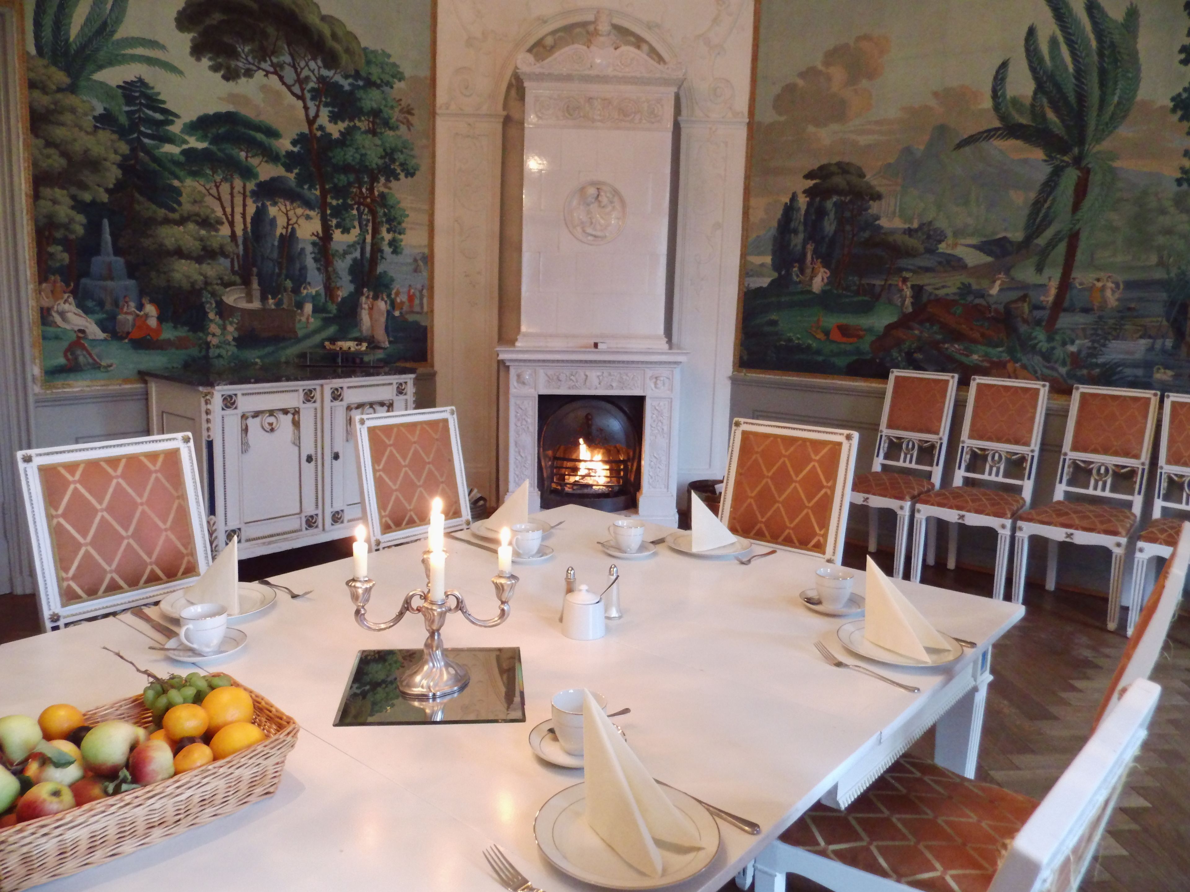 A formal dining room with a long table set for a meal, surrounded by chairs with patterned cushions. A candelabra with candles is placed in the center of the table.
