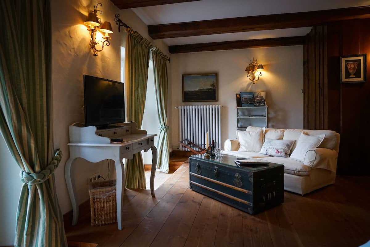 Una sala de estar acogedora con un sofá blanco, una mesa de centro de cristal, un televisor sobre un mueble blanco y un baúl antiguo.