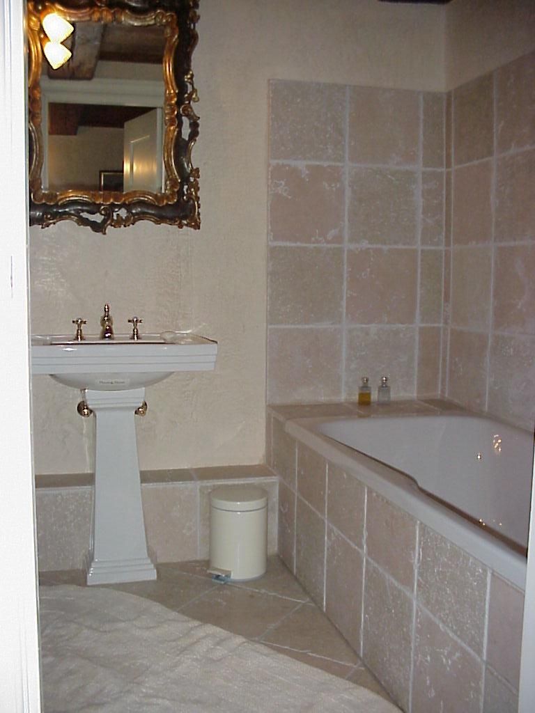 Een badkamer met een wastafel op een voetstuk, een bad en een spiegel met een sierlijk lijstwerk.