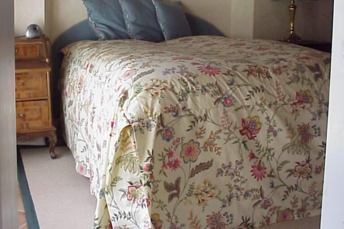 Un dormitorio con colcha estampada, un aparador de madera y una mesita de noche con lámpara.