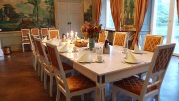 Uma sala de jantar com uma mesa comprida posta para refeição, rodeada por cadeiras com assentos acolchoados.