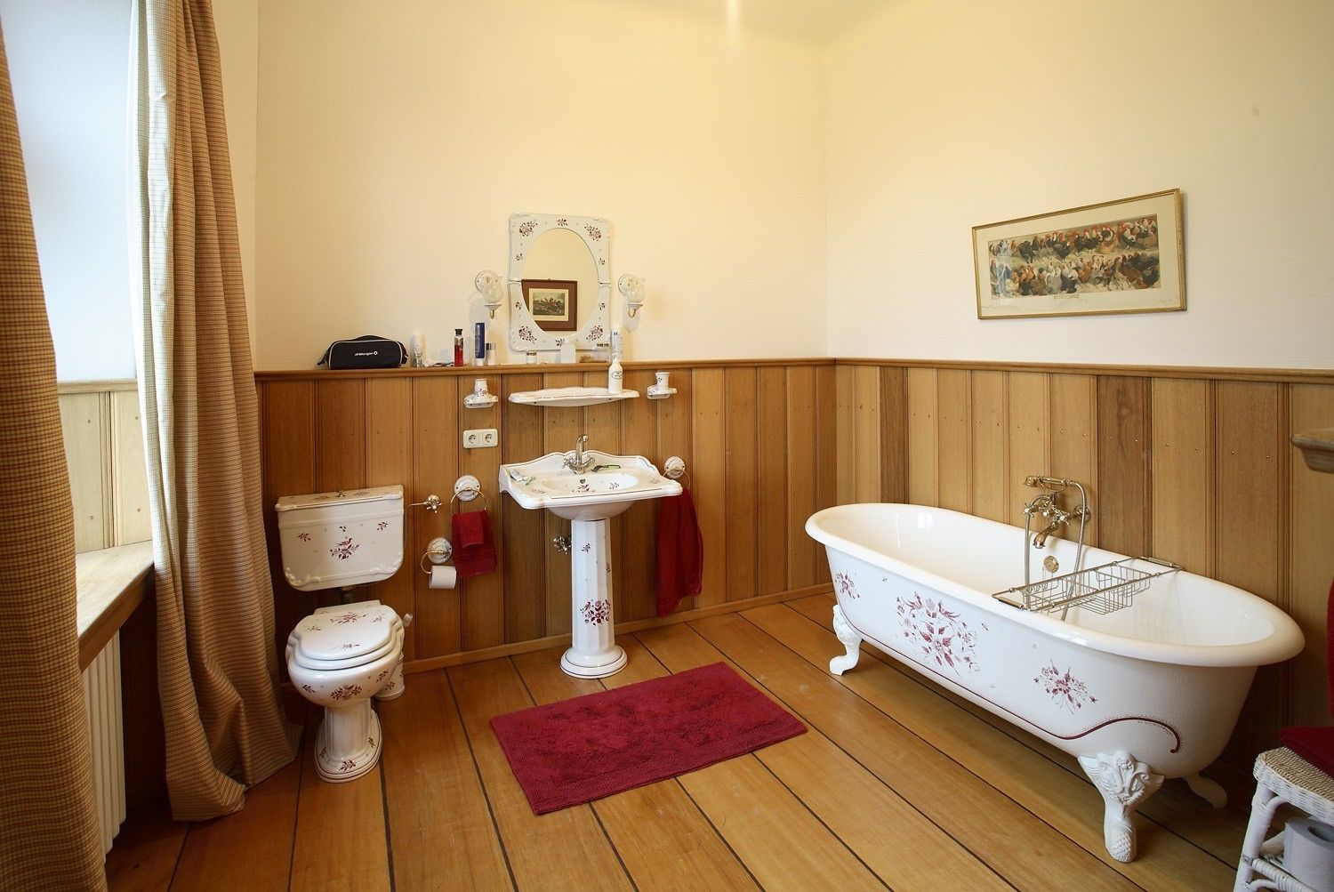 Une salle de bain avec un plancher en bois, une baignoire blanche, un lavabo blanc, des toilettes et un miroir.