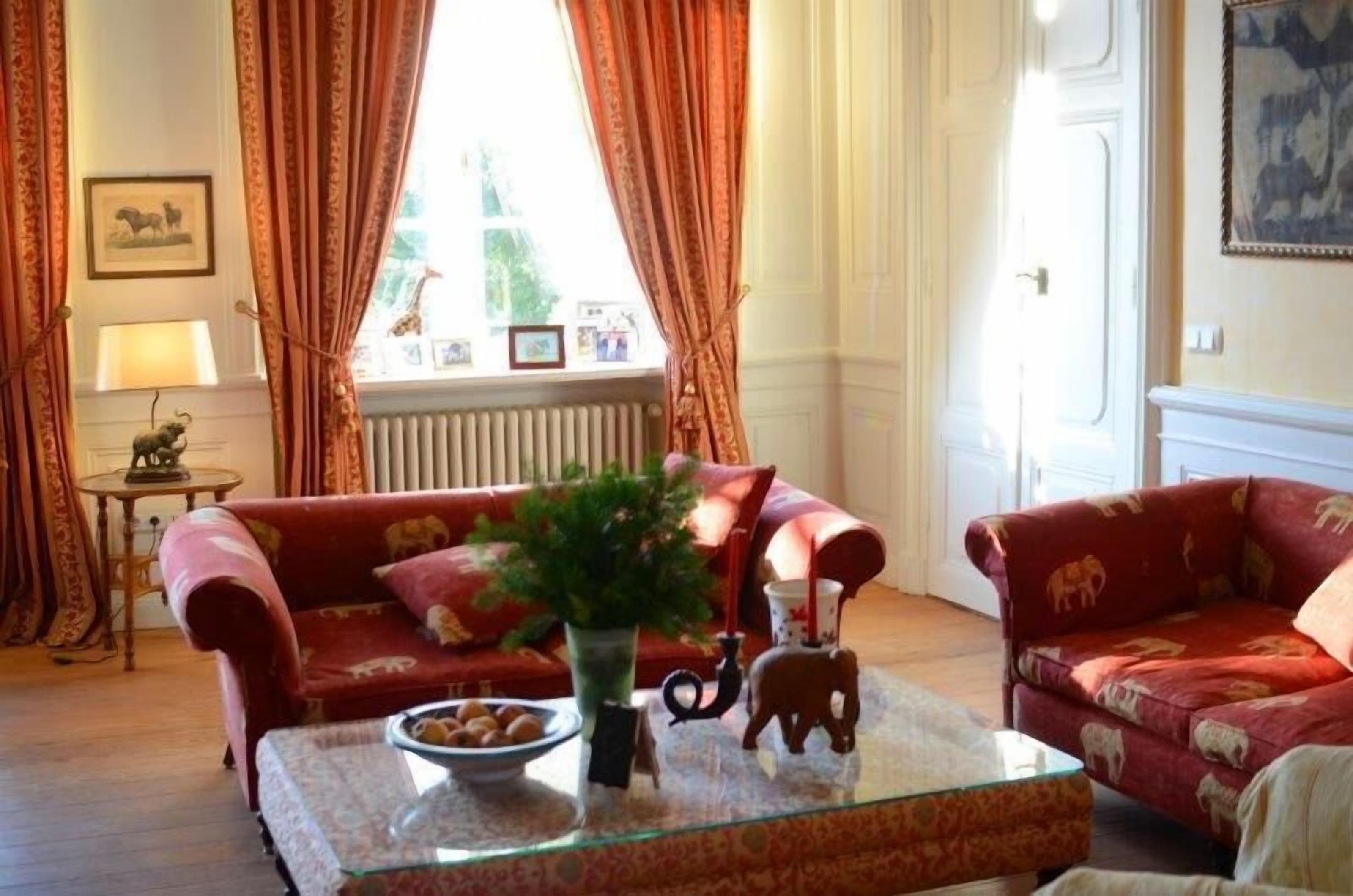 A living room with two red sofas, a glass coffee table with decorative items, and a window with curtains.