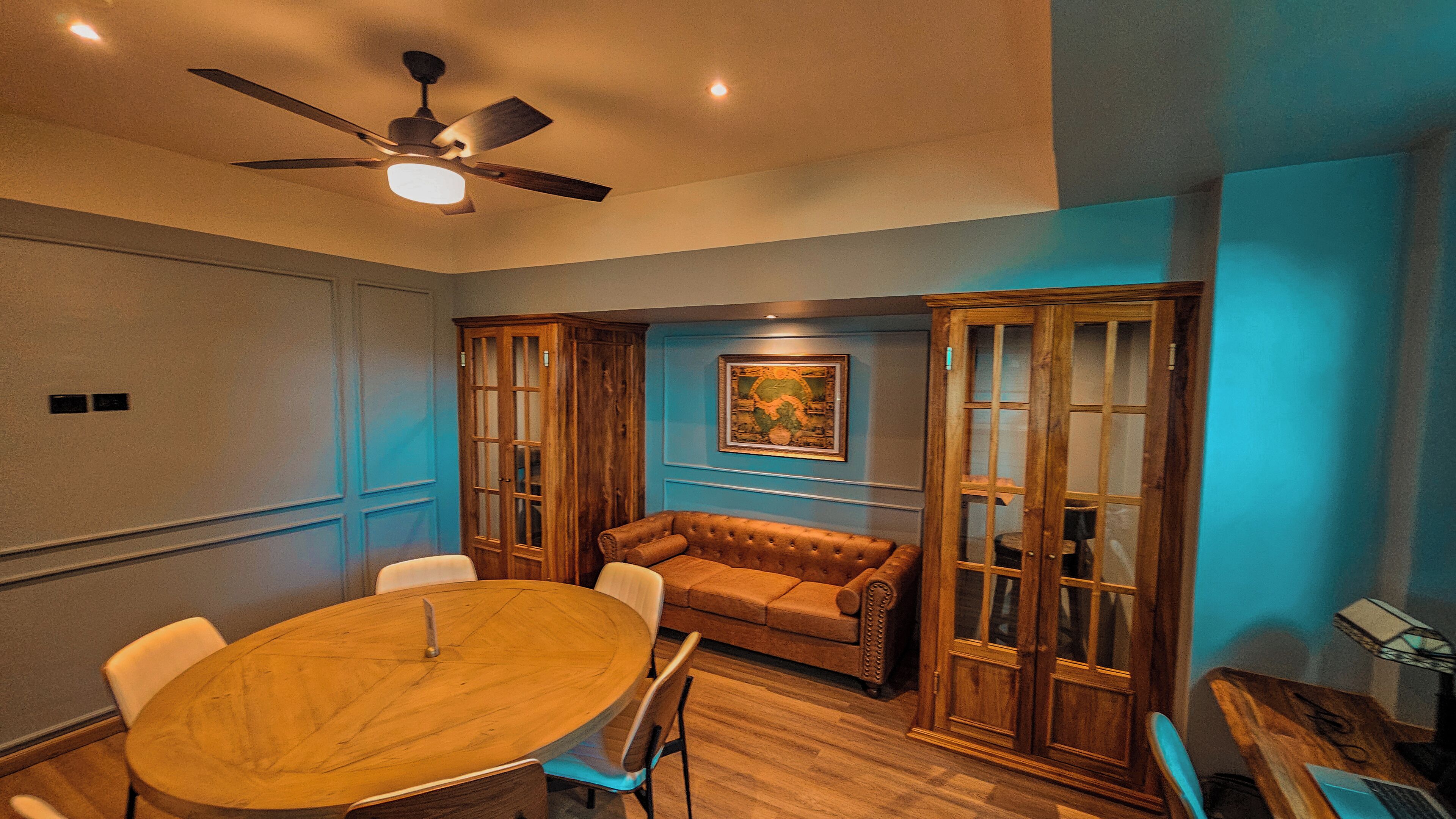 Una sala de conferencias con una mesa de madera, sillas blancas, un sofá marrón y armarios de madera.