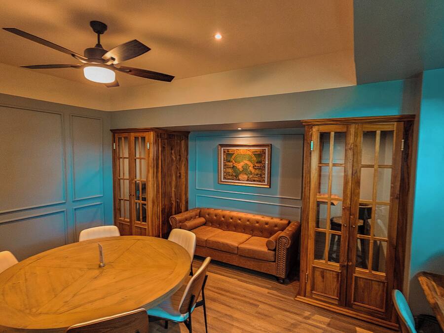 Una sala de conferencias con una mesa de madera, sillas blancas, un sofá marrón y armarios de madera.