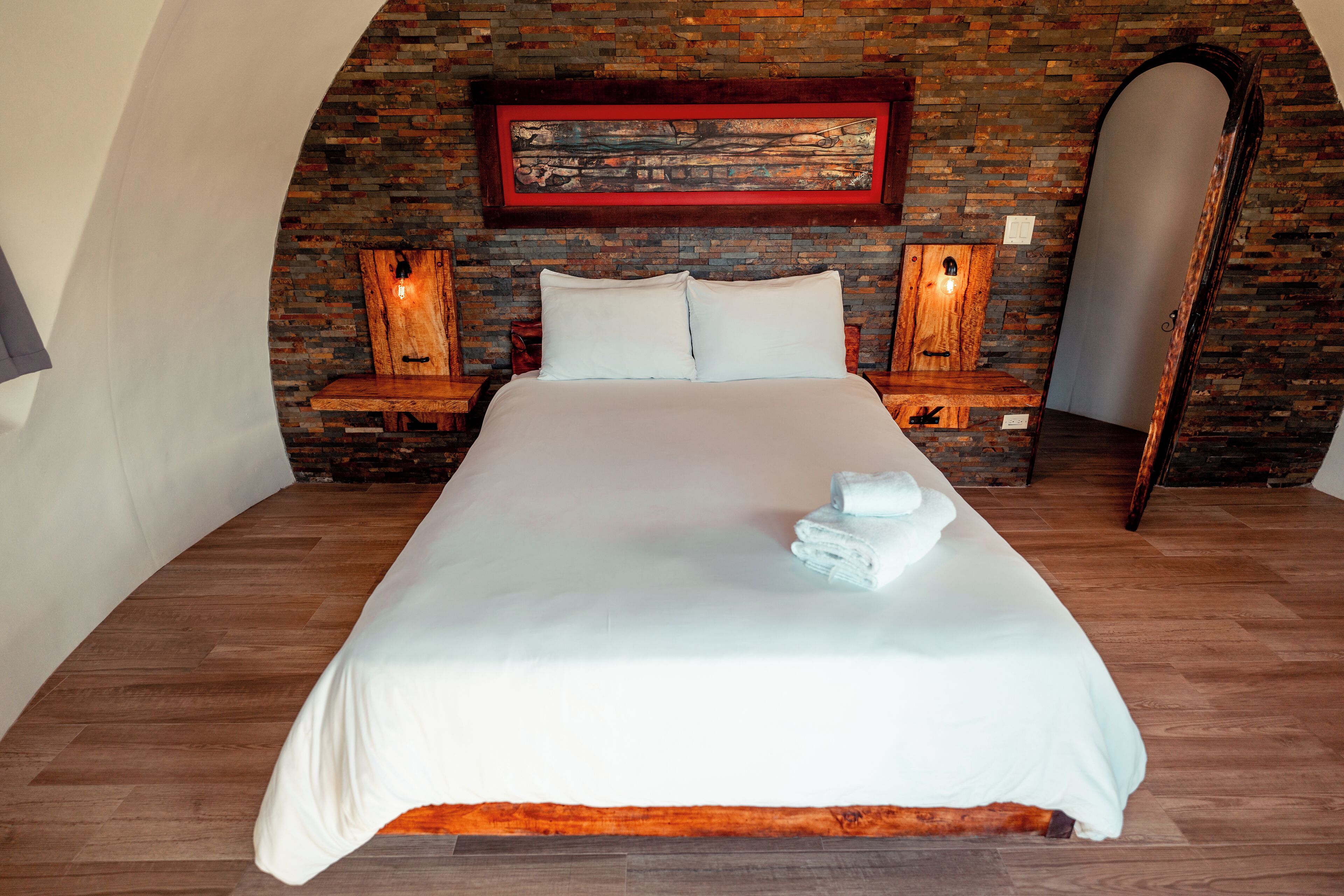 A bedroom with a large bed, wooden headboard, and a brick wall.