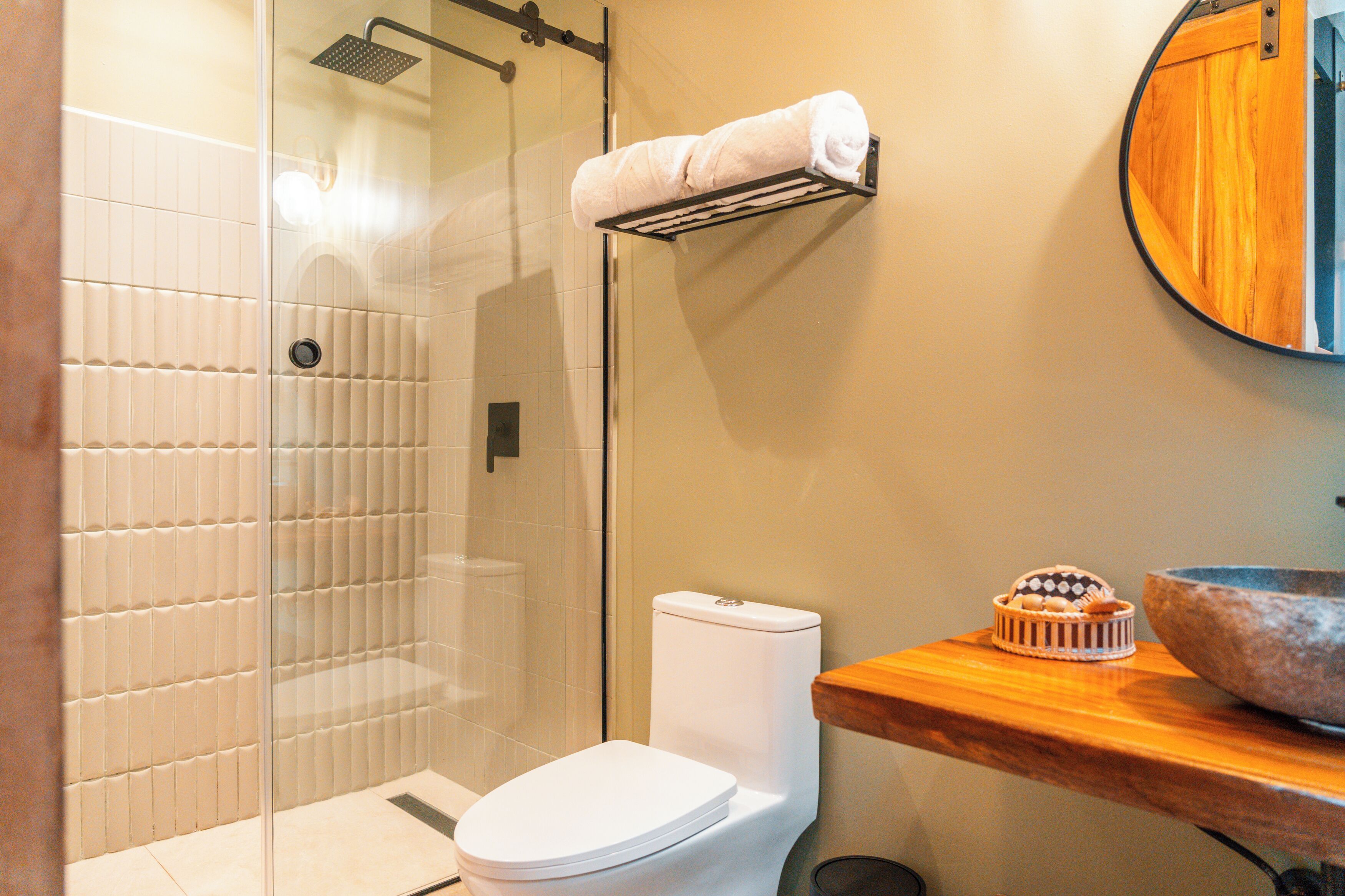 A bathroom with a glass-enclosed shower, a white toilet, and a wooden vanity with a bowl sink.