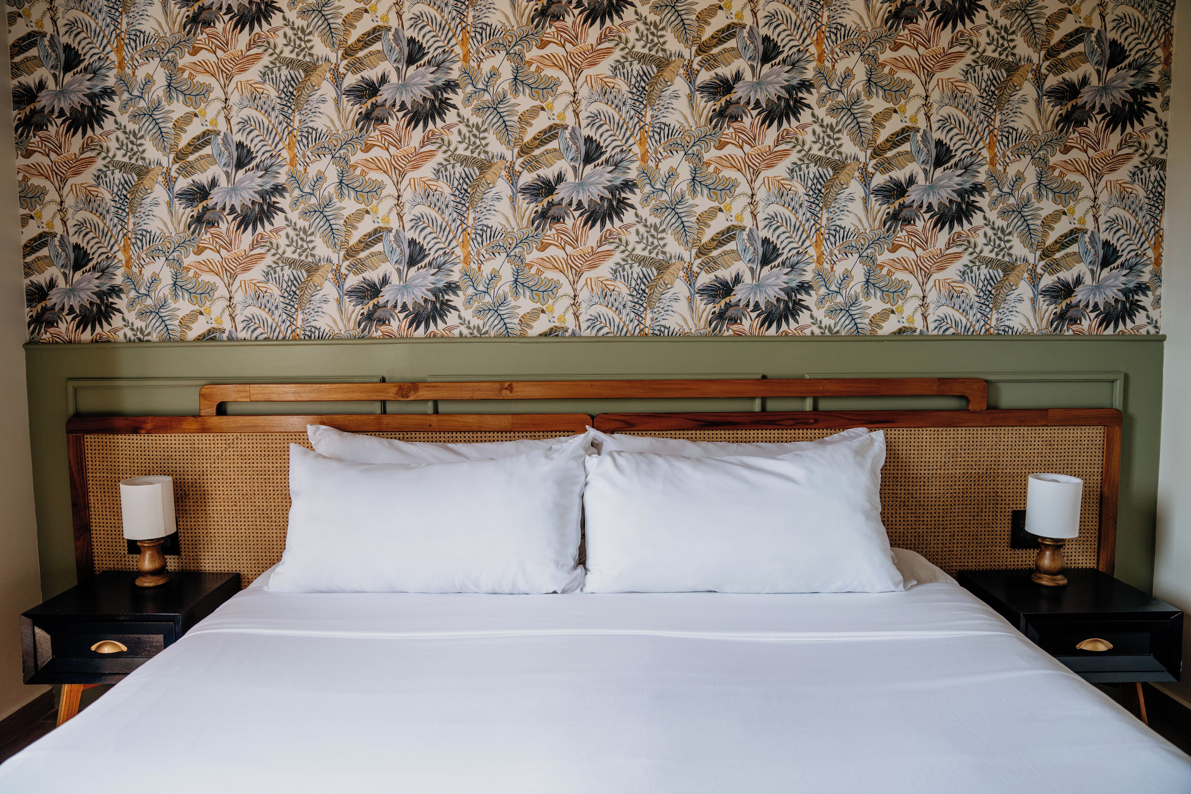 A hotel room with a large bed, two bedside tables, and a floral-patterned wallpaper.