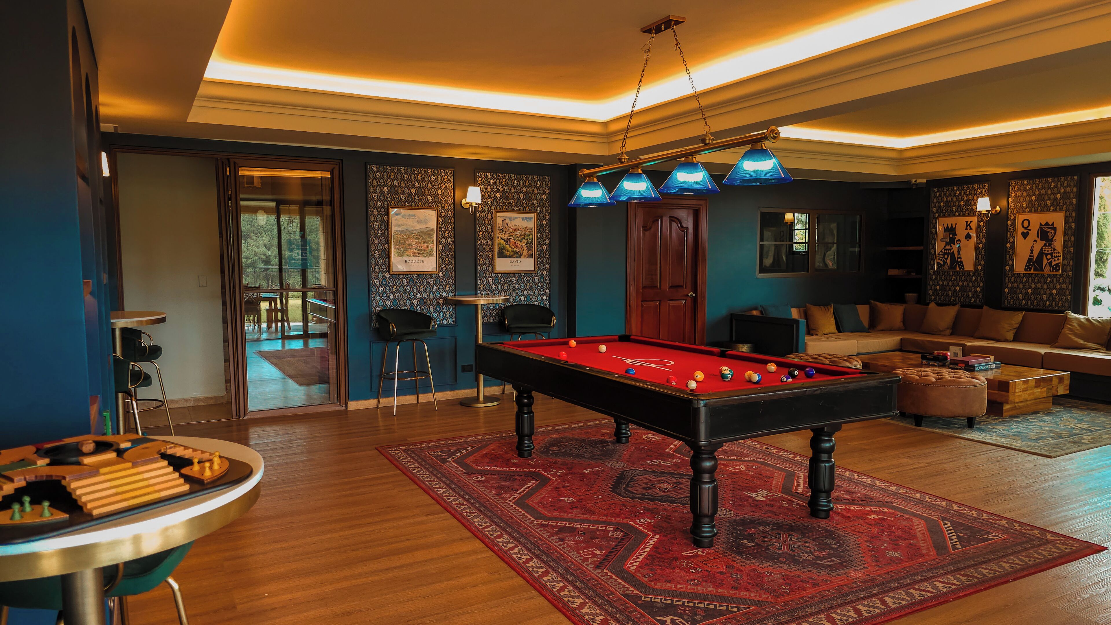 A pool table in a room with a red carpet, a sofa, and a bar area.