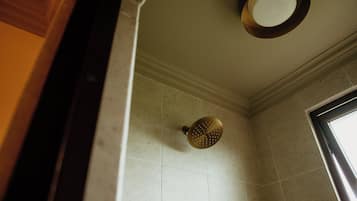 Un baño con cabezal de ducha en la pared, un espejo encima y una ventana a la derecha.