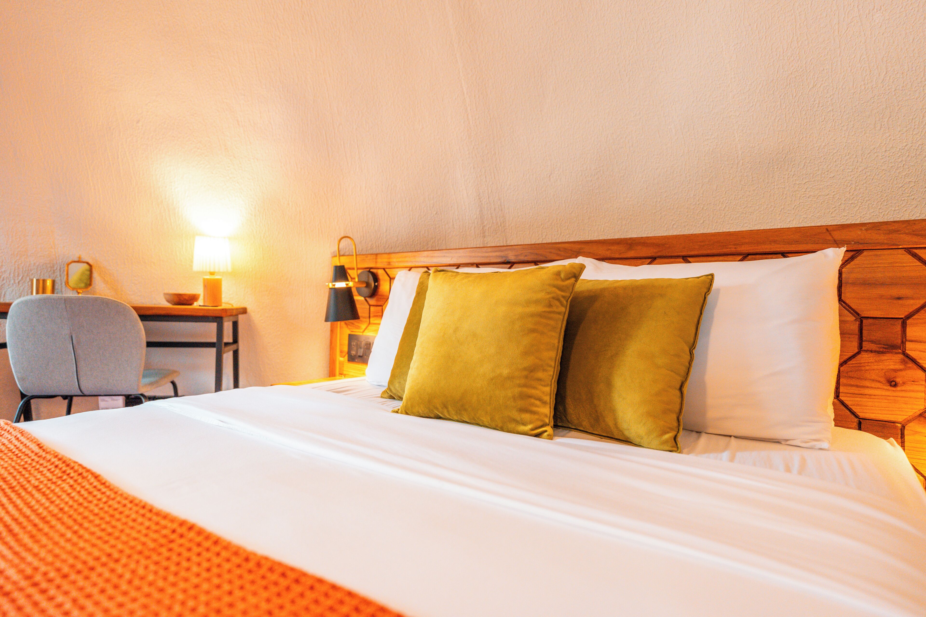 A neatly made bed with white and green pillows, a wooden headboard, and a bedside table with a lamp and a small decorative item.