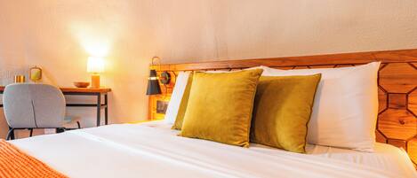 A neatly made bed with white and green pillows, a wooden headboard, and a bedside table with a lamp and a small decorative item.