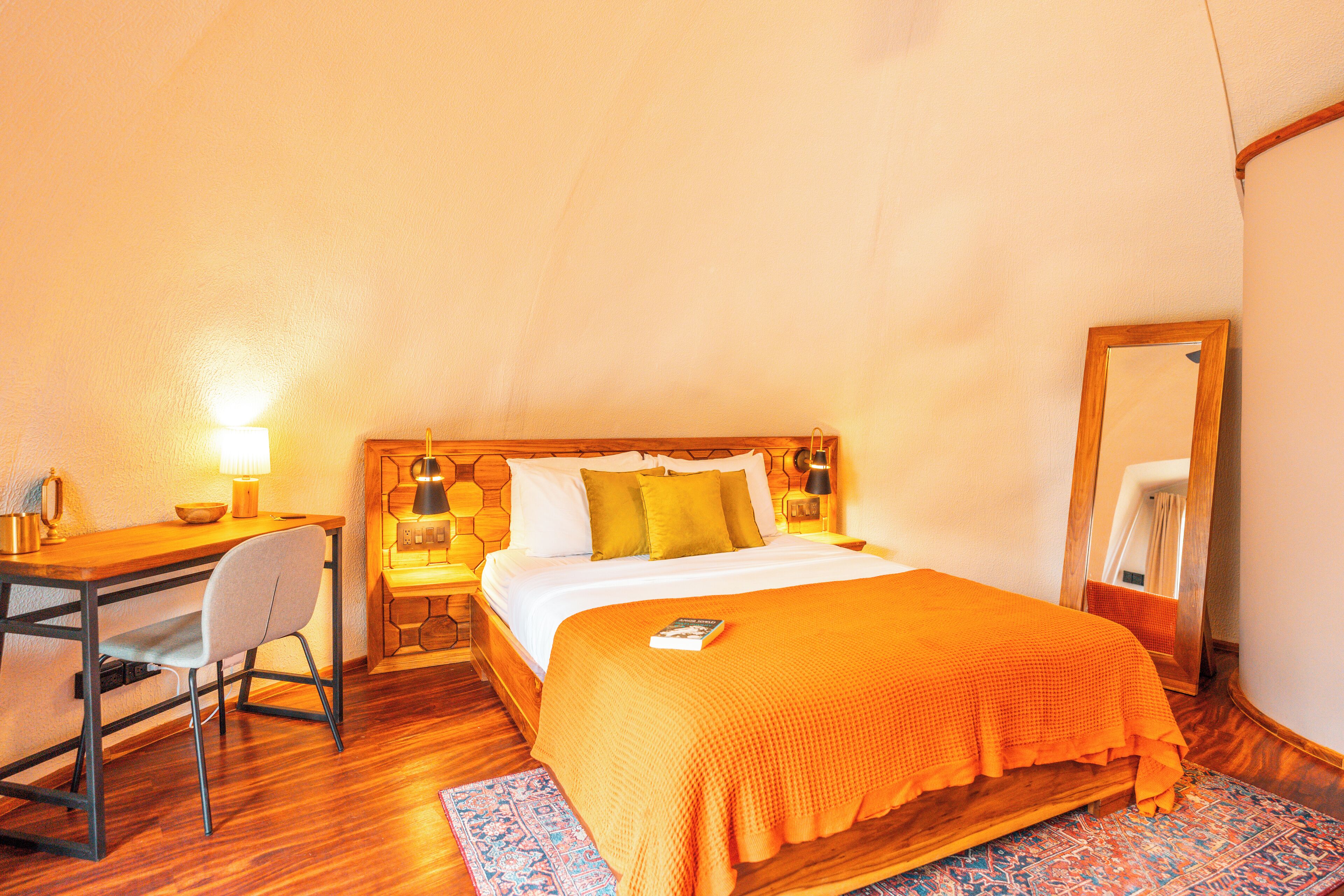 A room with a bed, a desk, a chair, and a nightstand with a lamp.