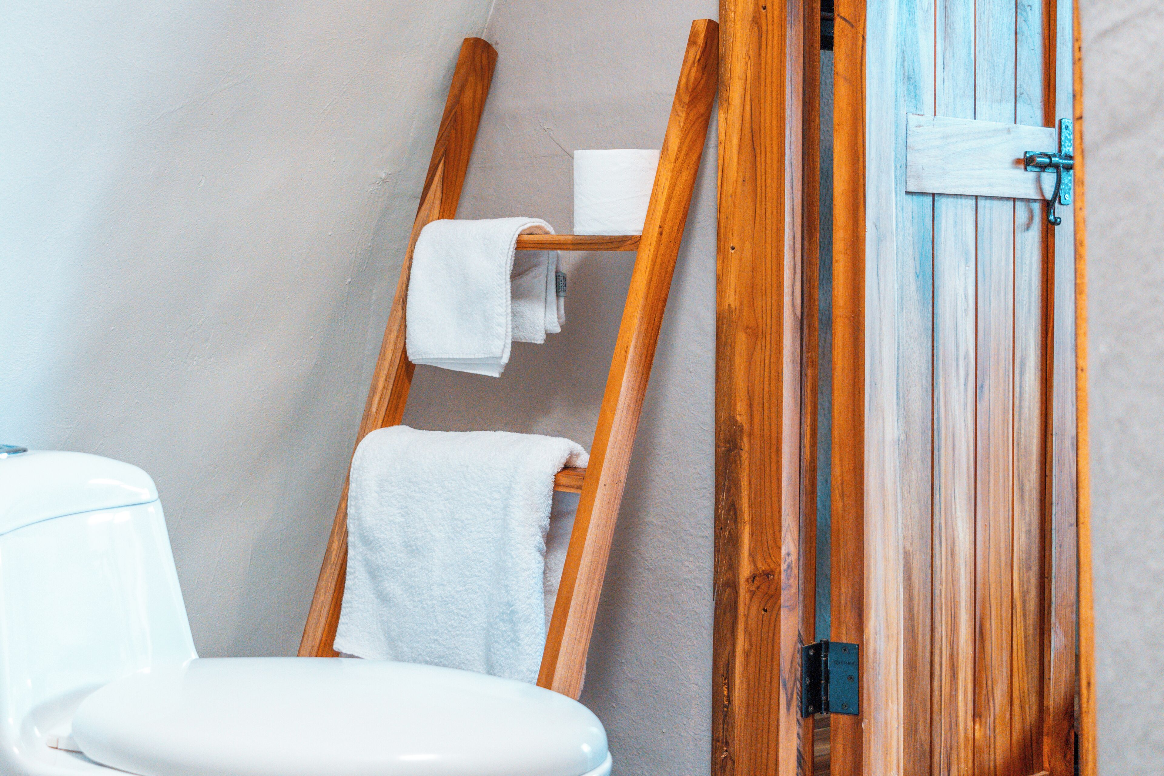 Un baño con una escalera de madera, un inodoro blanco y una puerta de madera.