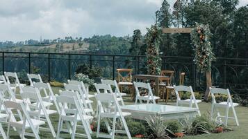 An outdoor wedding setup with white chairs arranged in rows, a table, and a floral arch.