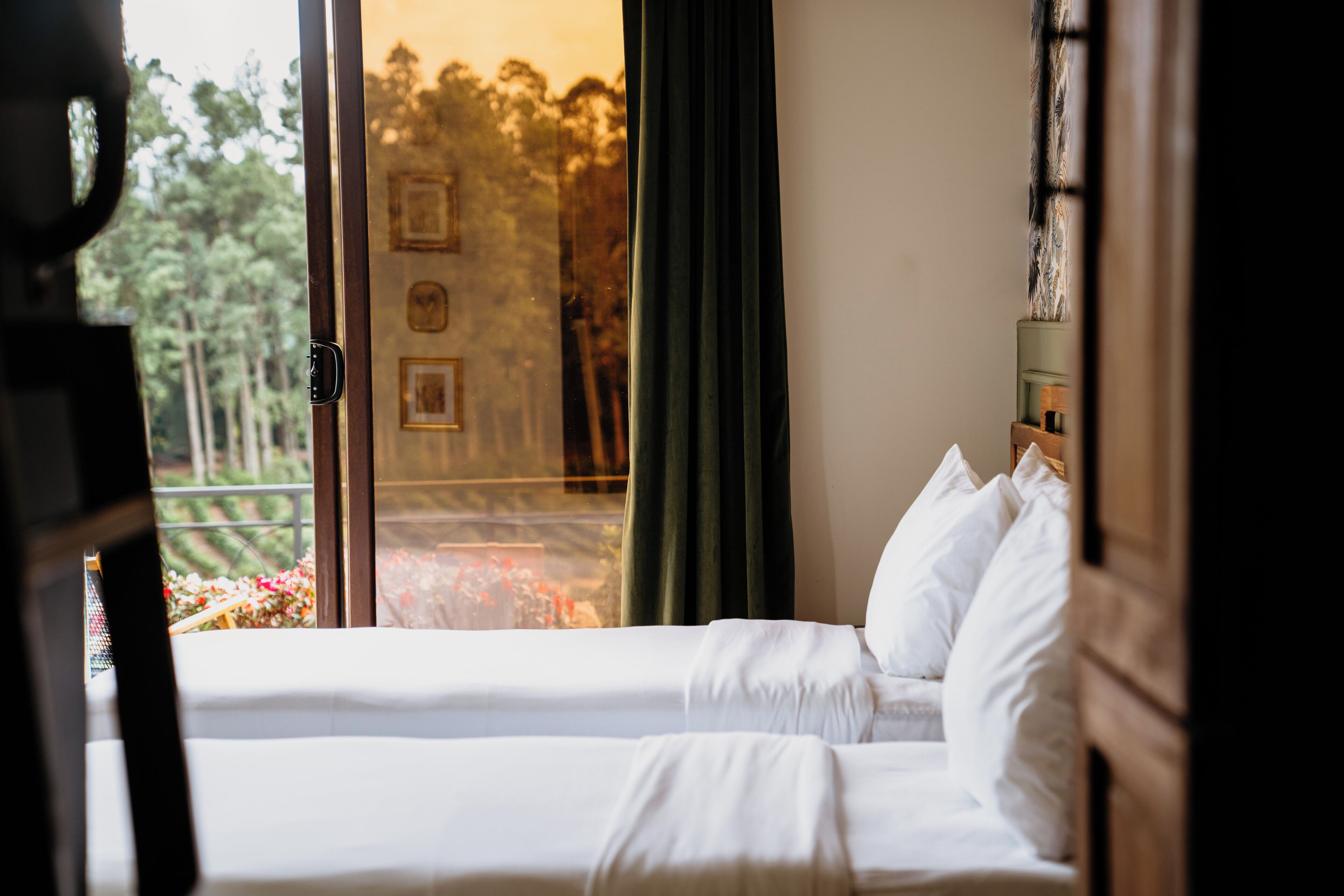 A hotel room with a bed, a view of trees through a window, and a door with a handle.