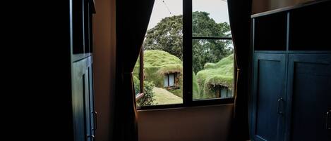 A room with a large window, wooden furniture, and a view of a lush garden.