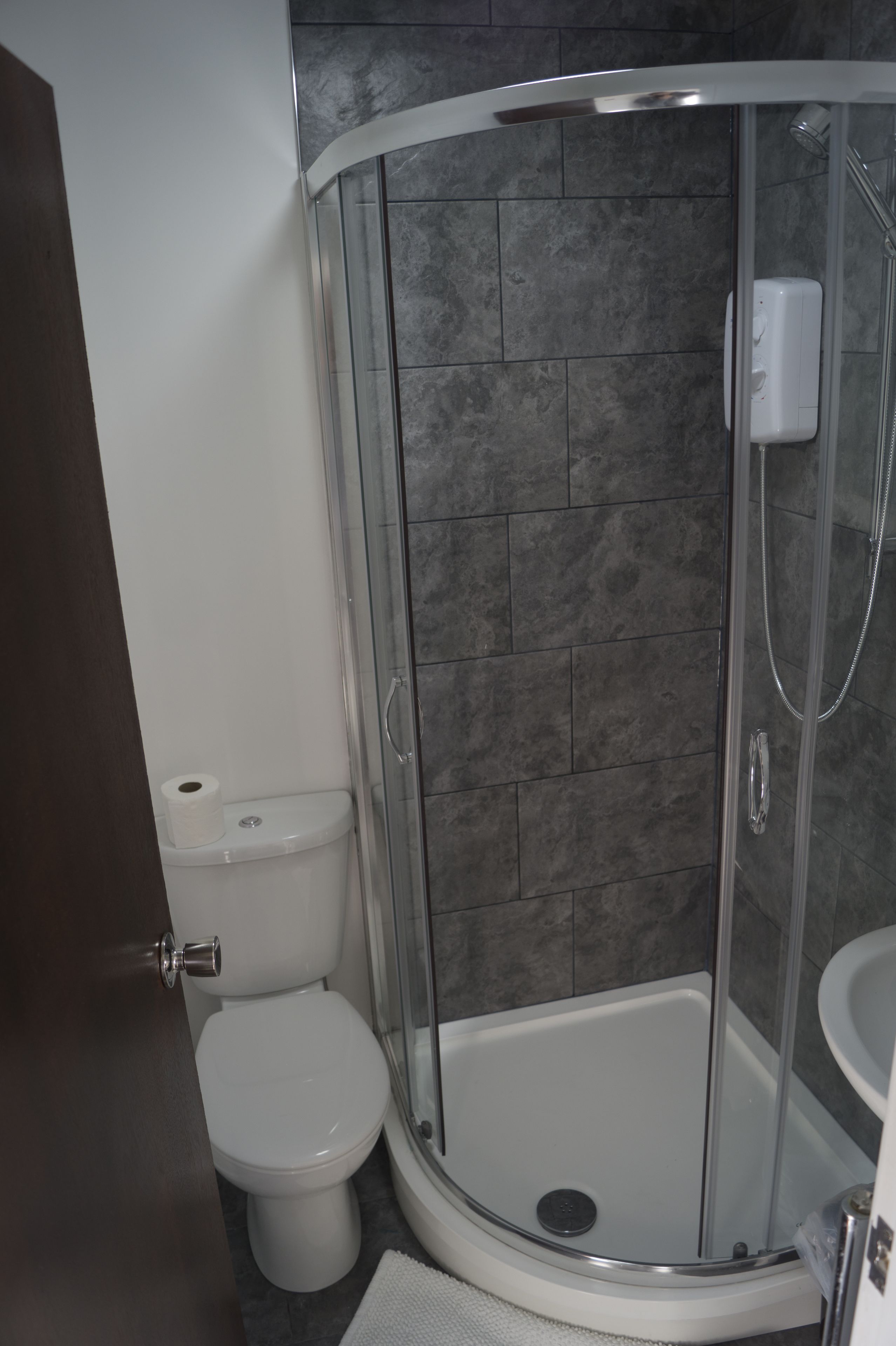 Une salle de bain avec une douche à parois de verre, des toilettes blanches et un sol carrelé.