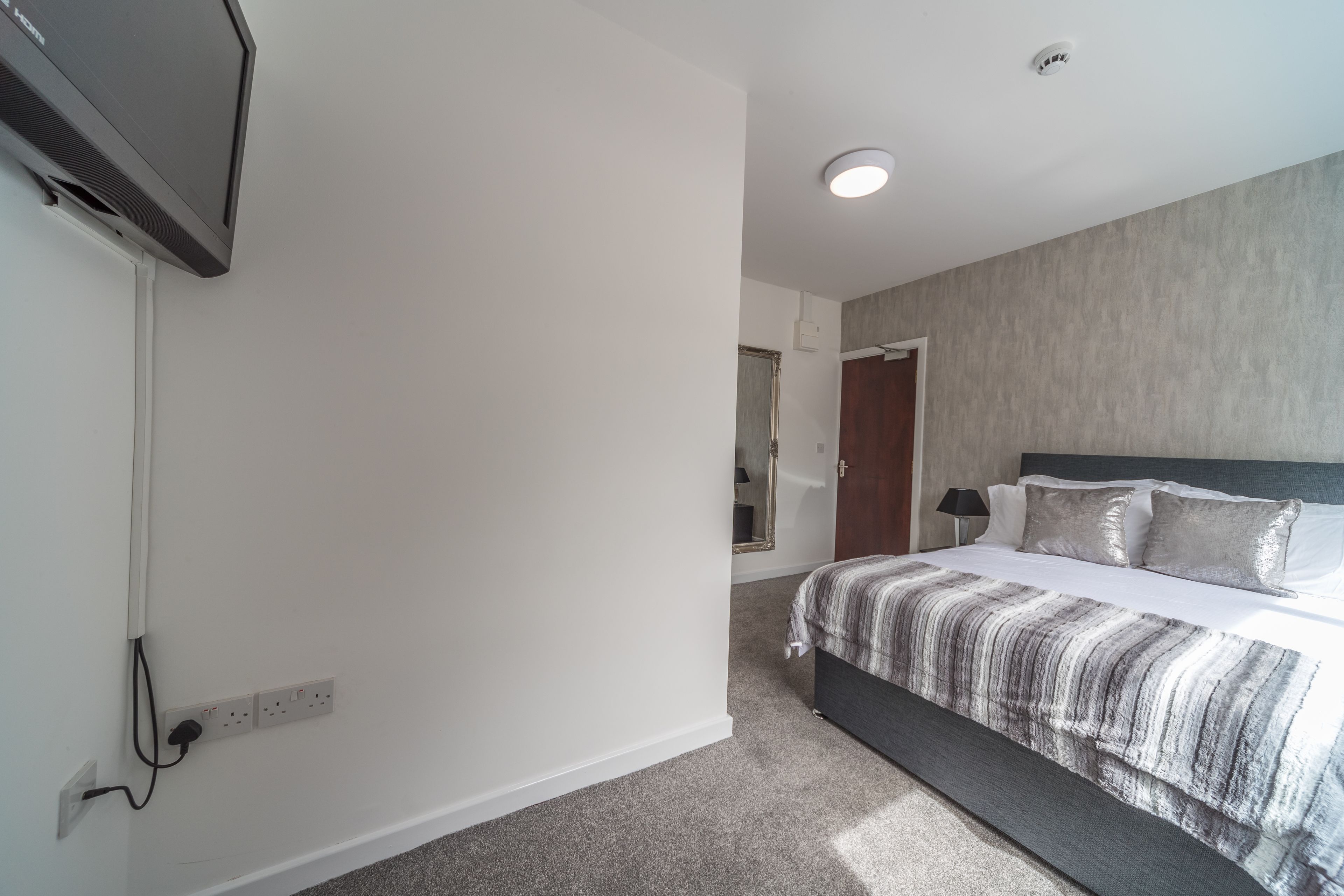 A modern bedroom with a large bed, a TV mounted on the wall, and a power outlet on the wall.