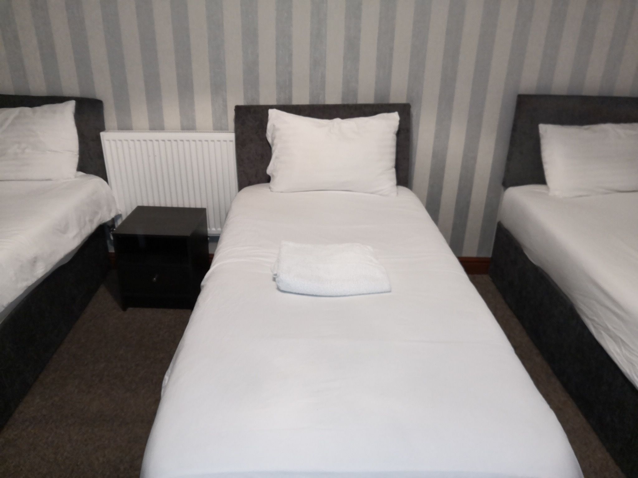 Et hotelværelse med to senge, et lille natbord og en radiator.