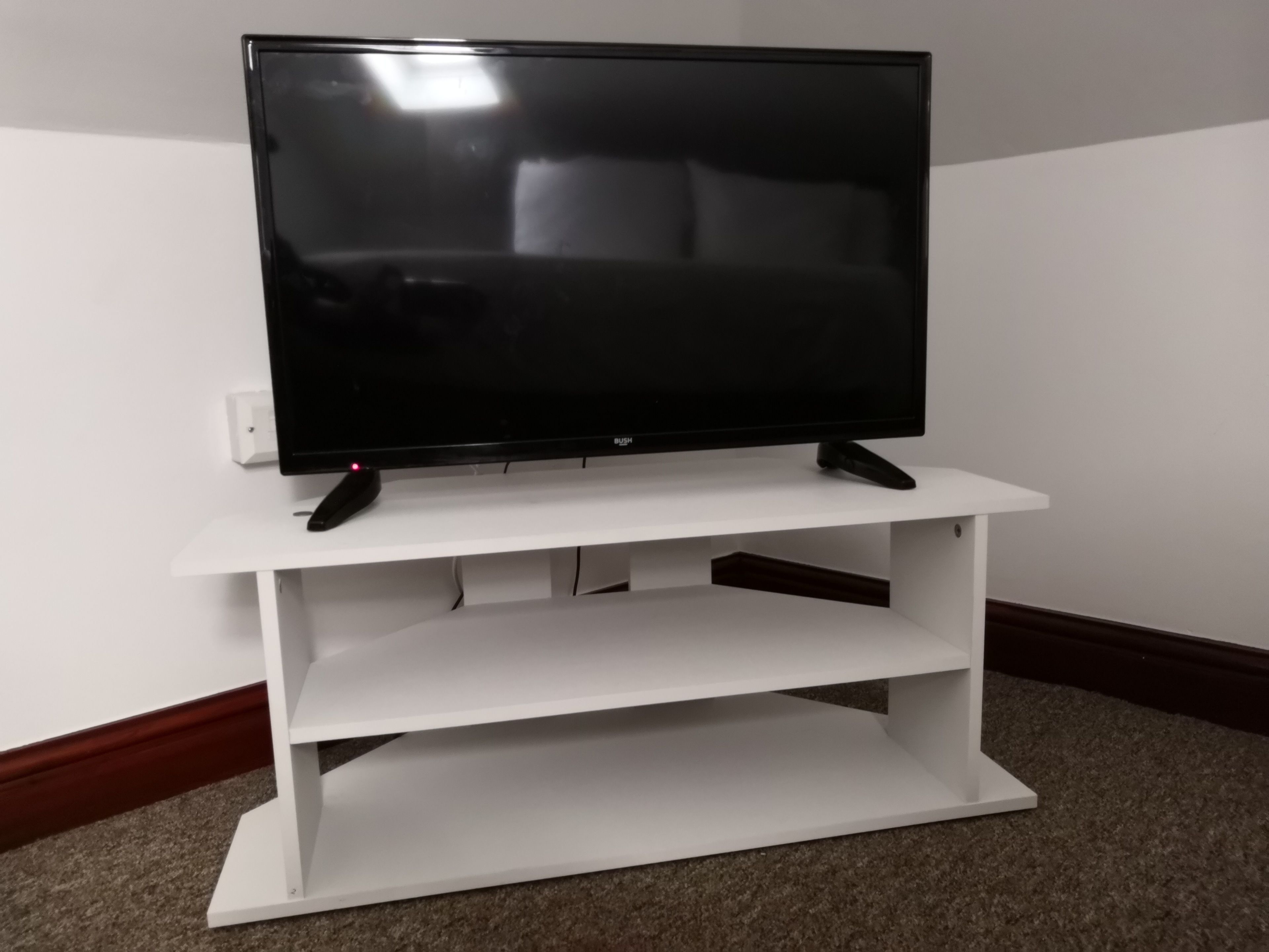 A flat-screen TV on a white TV stand with a remote control on it.