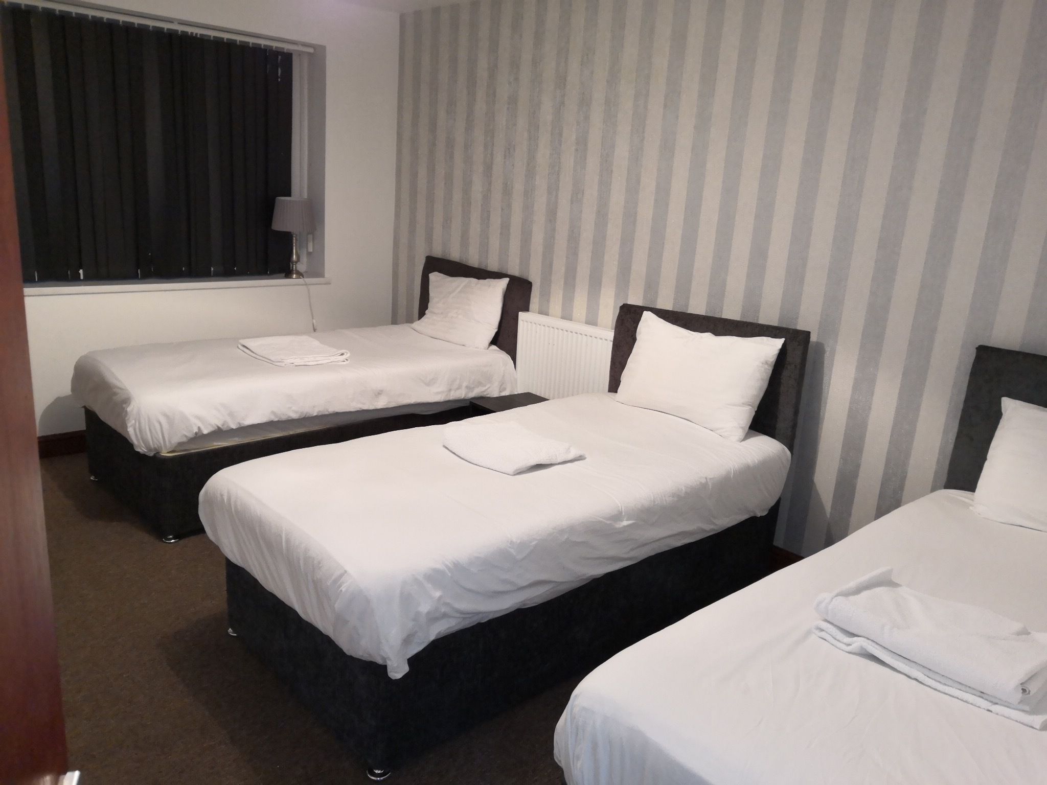 A hotel room with two single beds, a window with curtains, and a striped wall.