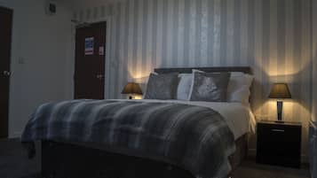 A neatly made bed with a striped blanket, two bedside lamps, and a door with a sign.