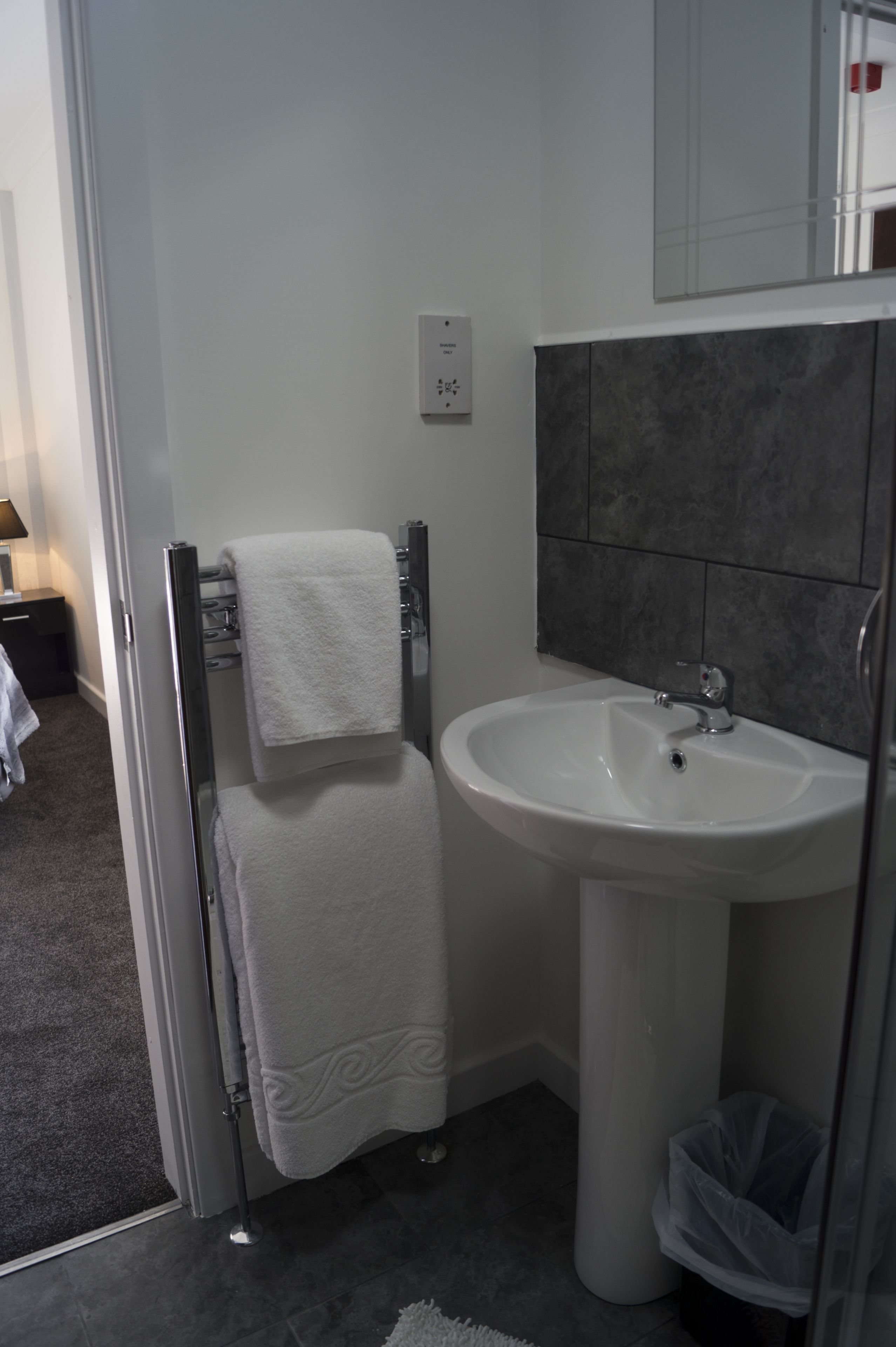 A bathroom with a white sink, a towel rack, and a trash bin.