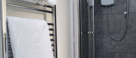 A shower area with a glass door, a white towel rack, and a white towel.