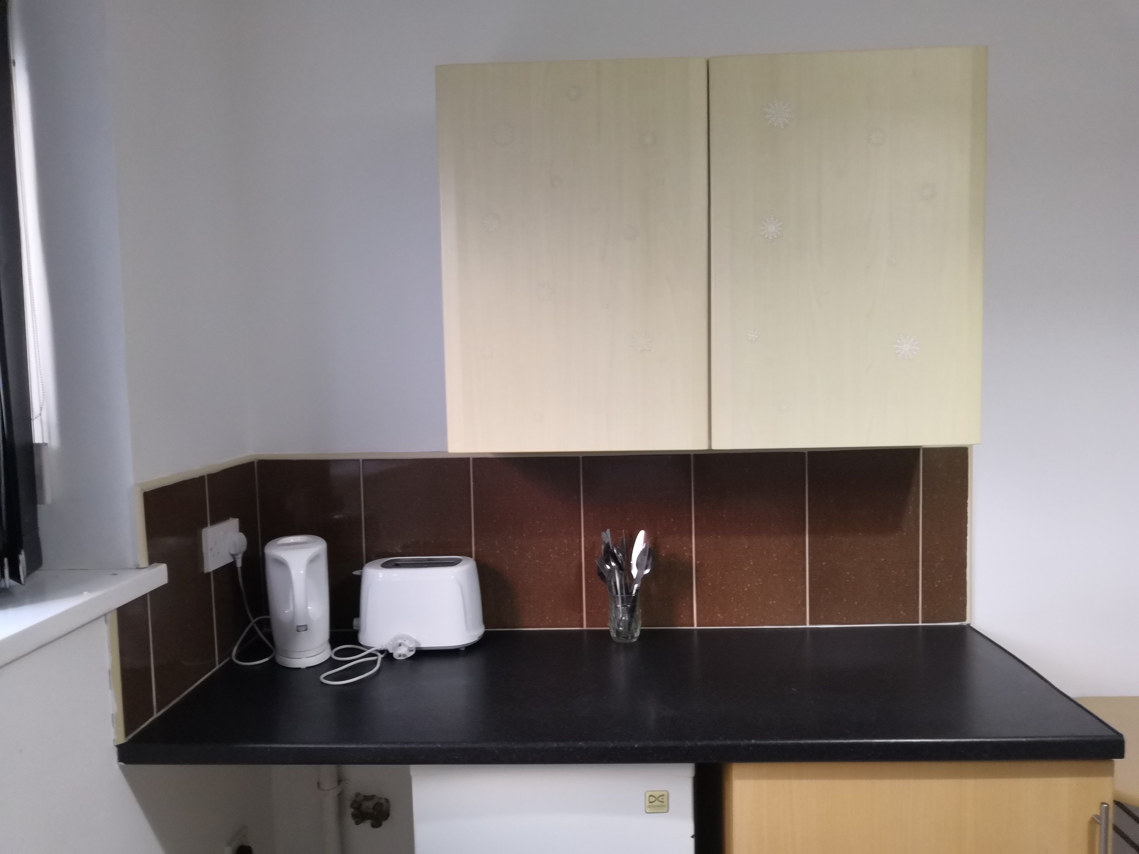 A kitchen with a black countertop, a toaster, a kettle, and a sink.