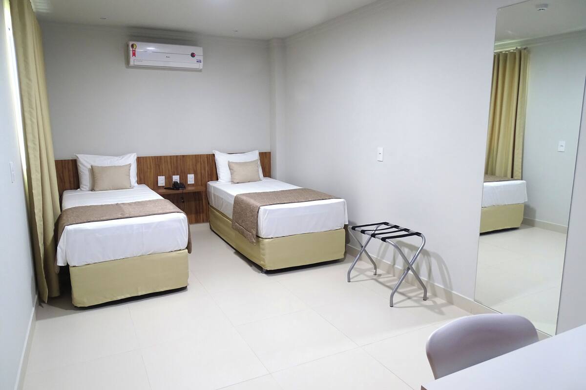 A hotel room with two beds, a small table, a chair, and a mirror.