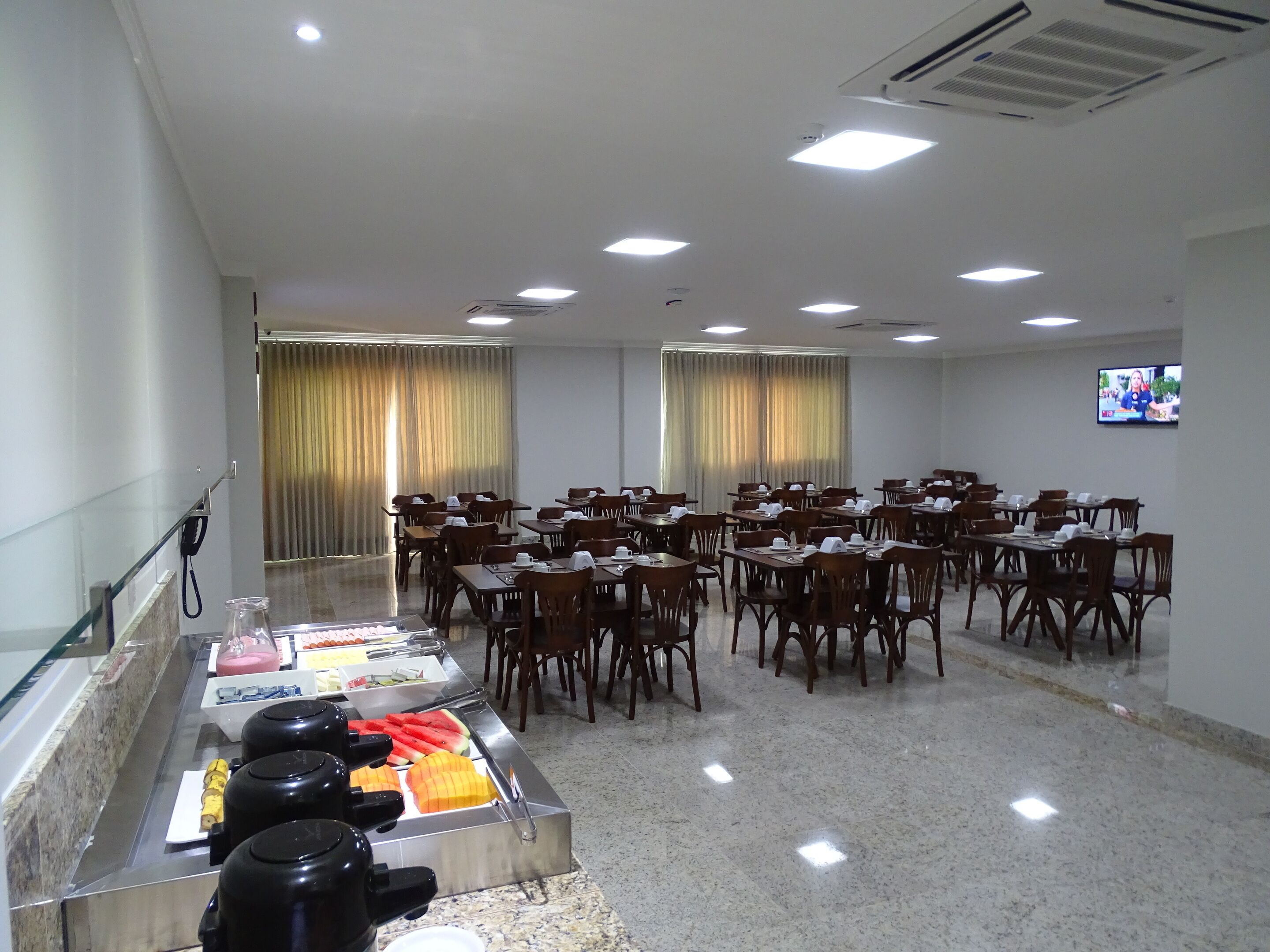 Un salón de conferencias con varias mesas y sillas, un área de buffet con diversos alimentos y una pantalla de televisión en la pared.