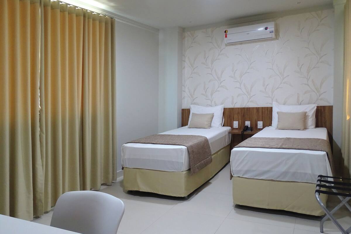 A hotel room with two beds, a desk, a chair, and an air conditioning unit on the wall.