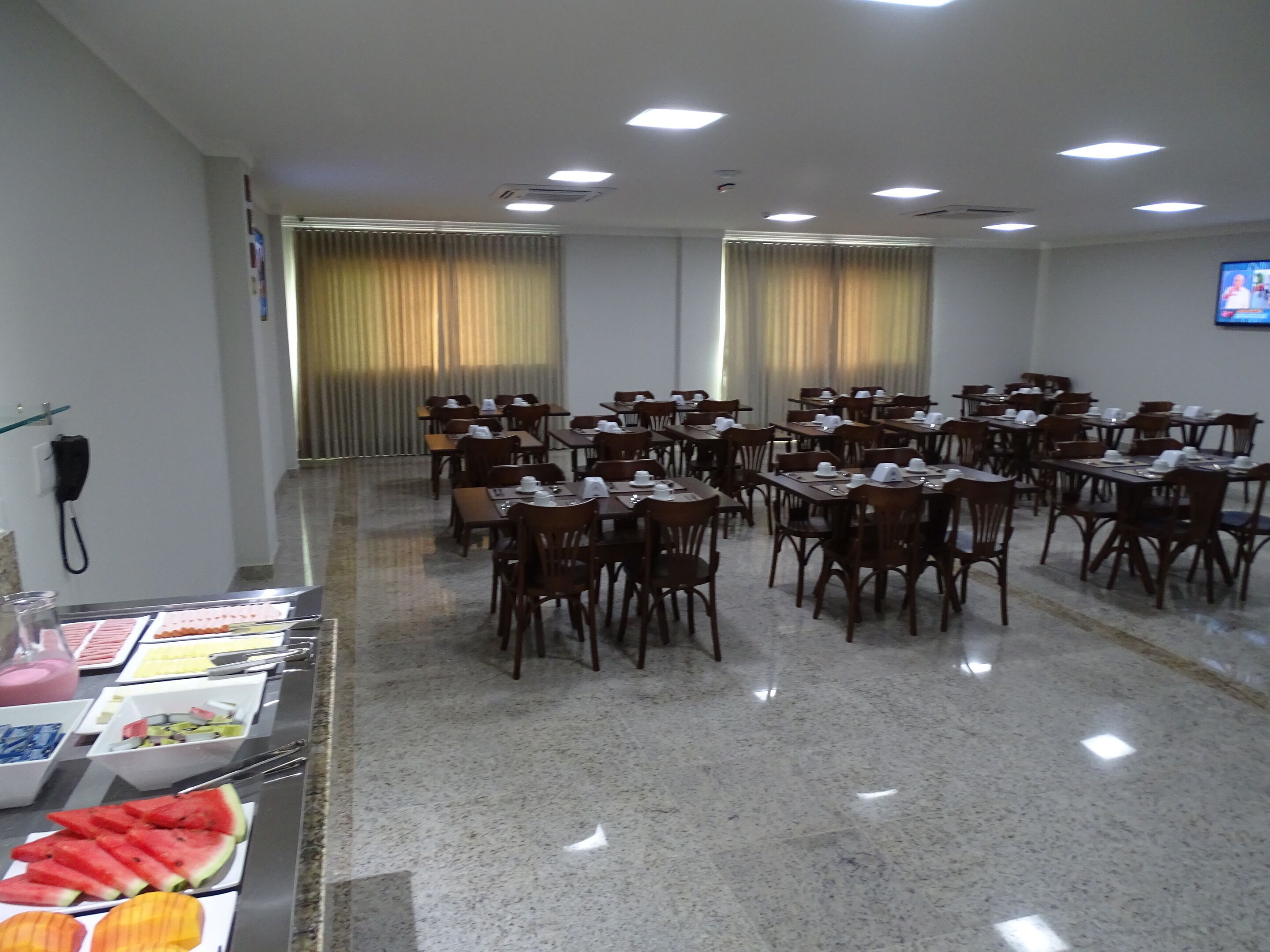 Una sala conferenze con numerosi tavoli e sedie, un'area buffet con diversi cibi e uno schermo televisivo a parete.
