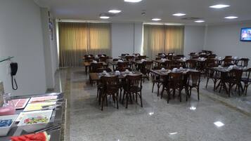 Una sala conferenze con numerosi tavoli e sedie, un'area buffet con diversi cibi e uno schermo televisivo a parete.