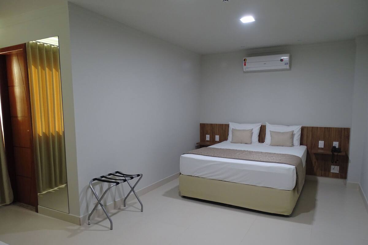 A hotel room with a bed, bedside table, and a small stool.