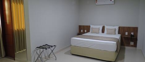 Una habitación de hotel con cama, mesita de noche y un taburete pequeño.
