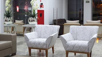 A modern lobby with two patterned armchairs, a red cabinet, and a glass wall with a reflection.